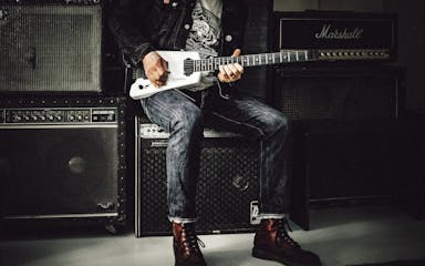 man wearing blue denim jeans playing white and black electric guitar sitting on black guitar amplifier