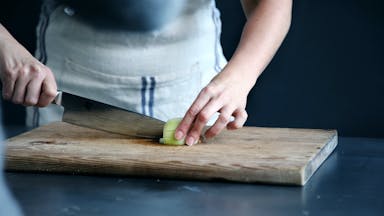 person slicing green vegetable on chopping board