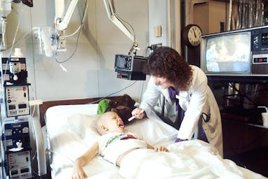 child lying on bed while doctor checking his mouth