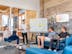 three men sitting while using laptops and watching man beside whiteboard