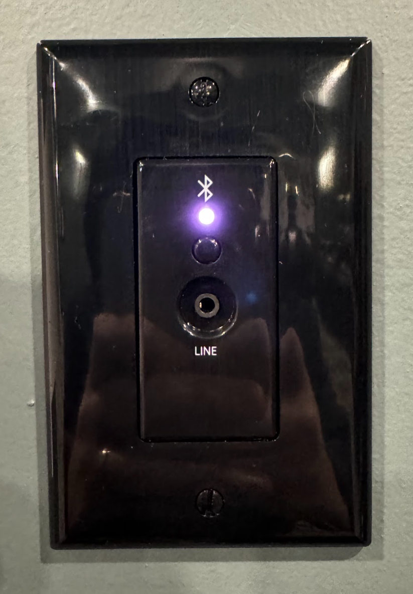 Bluetooth wall plate. Below the Bluetooth logo there is an LED, in this image purple. Below the LED is a button for Bluetooth pairing. Below the button is a 3.5mm audio input jack labelled "LINE".