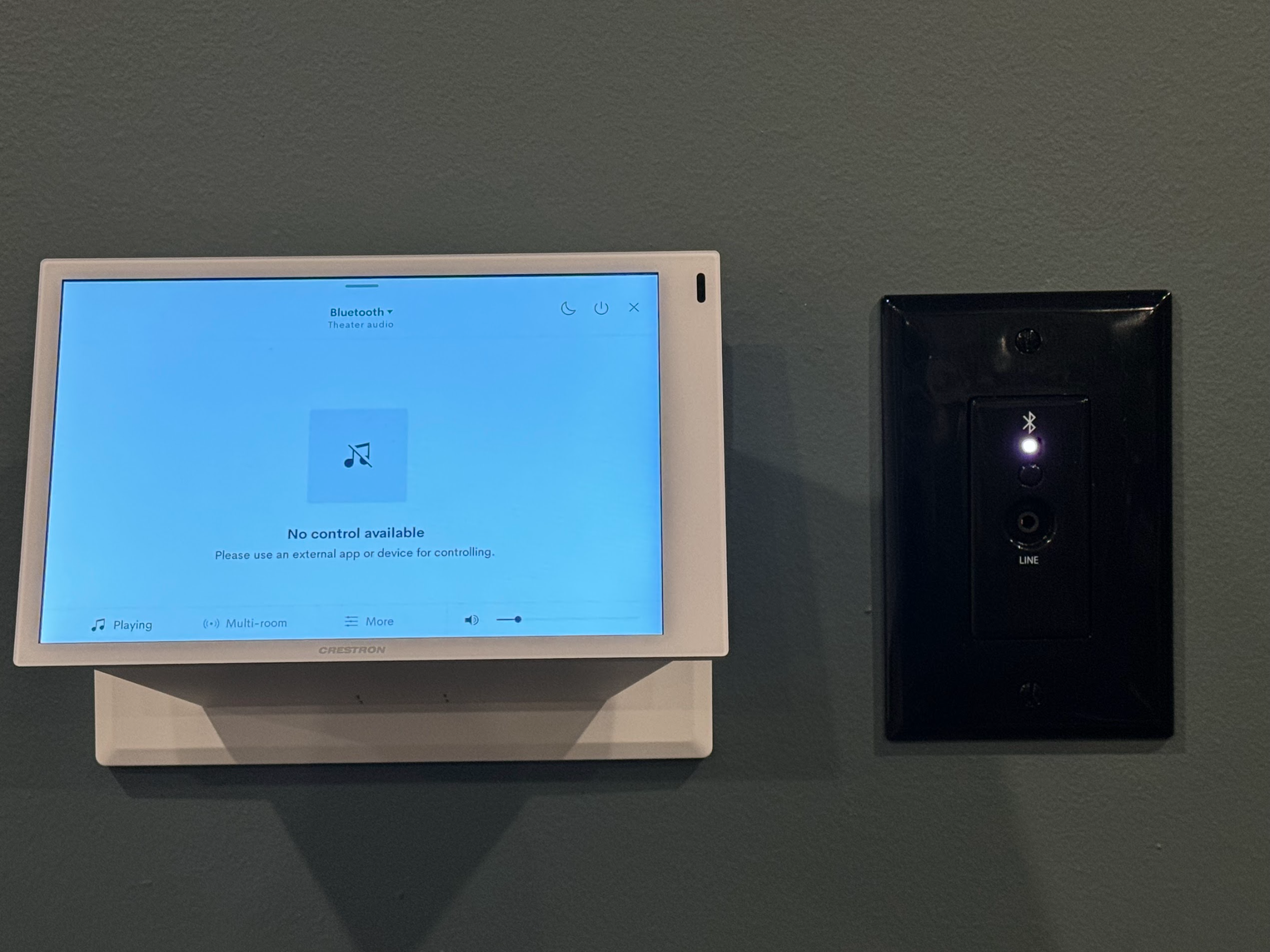 Image of a control touchscreen and Bluetooth wall plate. The touchscreen shows Bluetooth as an audio source, controlled externally. The Bluetooth plate has a white LED, indicating a device is paired.