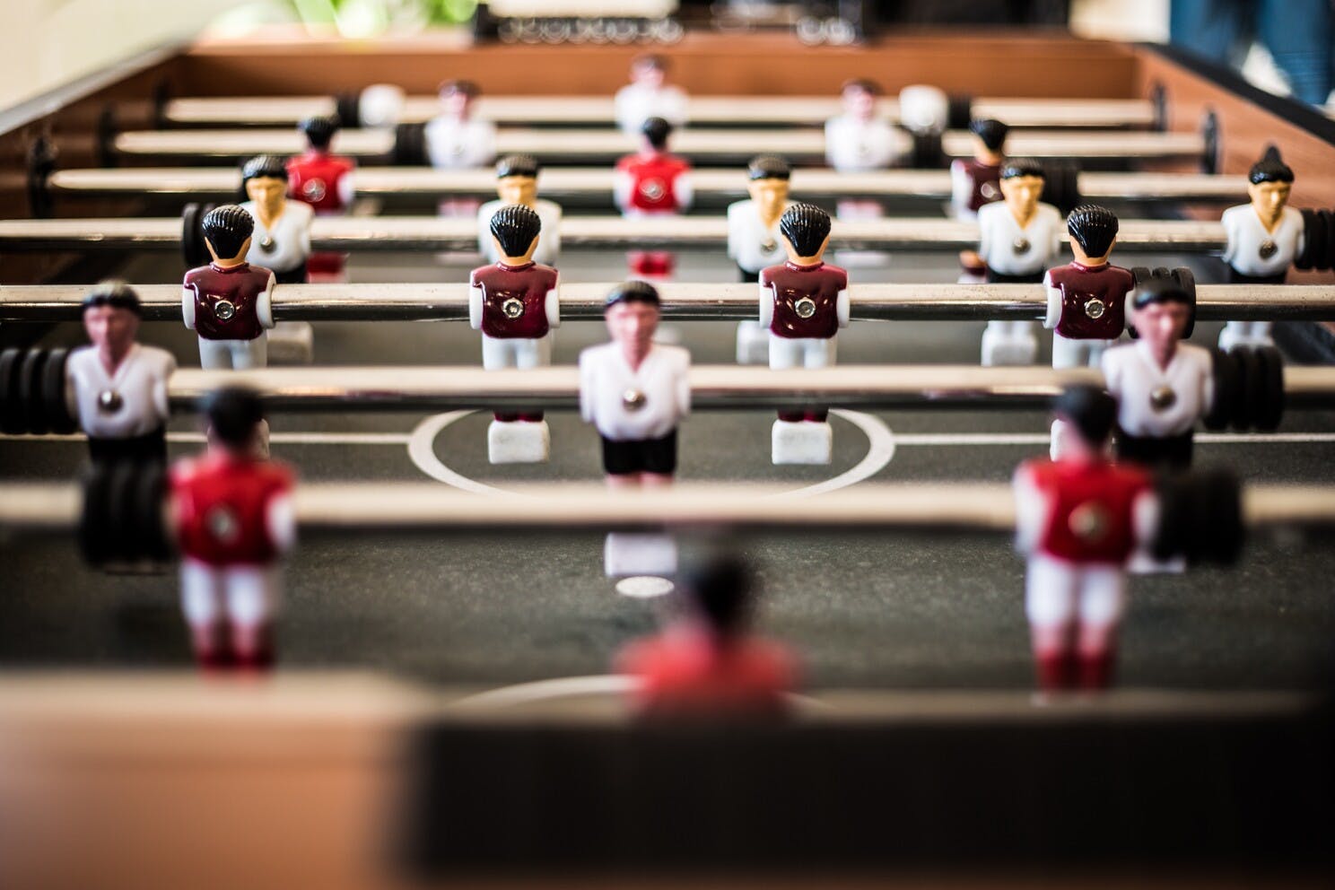 Muestra una vista rasante de la superficie de la mesa de futbolito, en la que los jugadores de plástico están sobre una barra cromada.