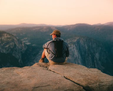 man in black t-shirt and brown hat sitting on rock