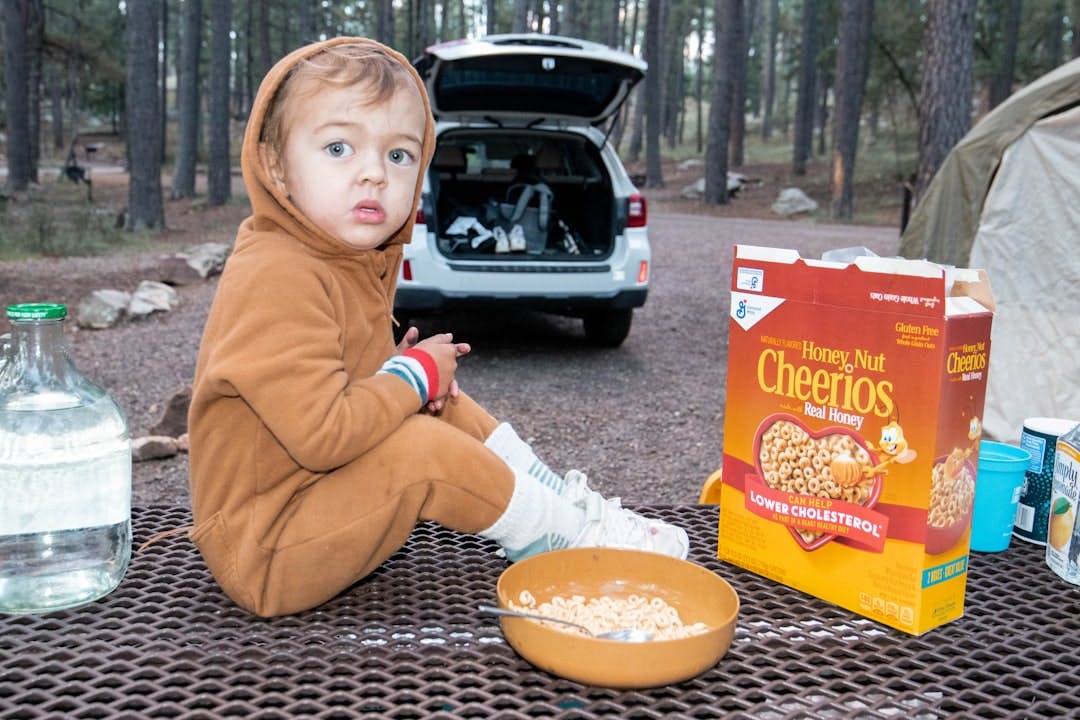 a young boy sitting on a picnic table next to a box of cereal